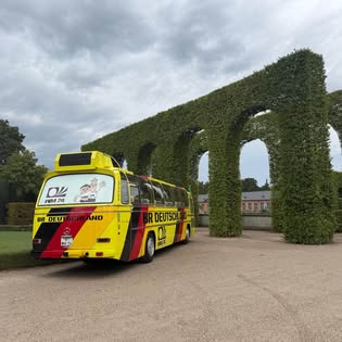 Autocar de collection sous une arche végétale, illustration de l'ambiance des rassemblements AAF
